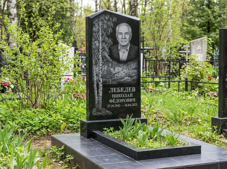 Памятник с гравировкой берёзы: вертикальная стела со скошенным верхом — берёза и стая птиц в небе, гранитный цоколь с тёмной плиткой, работа «Лебедев» в Норильске
