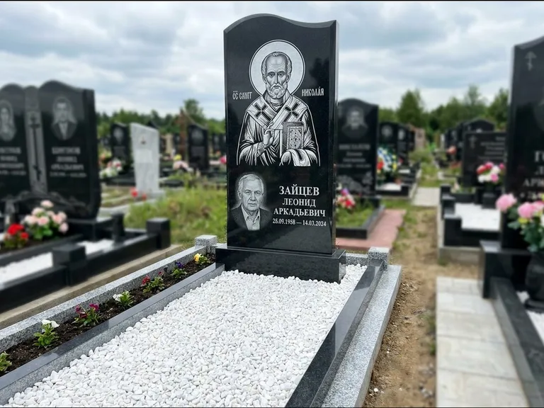 Памятник с гравировкой иконы: стела с крестообразным навершием — икона в резной рамке-киоте, газон без ограды, стриженая трава, работа «Раевская» в Норильске
