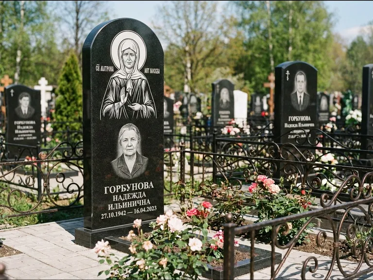 Памятник с гравировкой иконы: стела с арочным верхом и киотом под образ — гравировка образа Матроны Московской, гранитный цоколь с тёмной плиткой, работа «Ковалёв» в Норильске