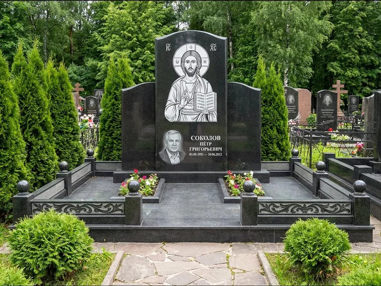 Памятник с гравировкой иконы: широкая горизонтальная лежачая плита-стела — икона в резной рамке-киоте, серая гравийная отсыпка с бордюром, работа «Богданова» в Норильске