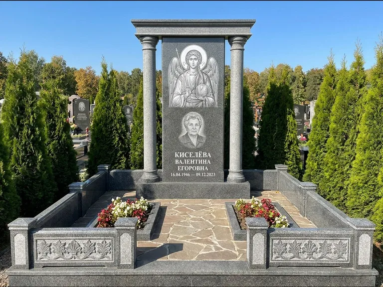 Памятник с гравировкой иконы: массивная стела с двускатным навершием-домиком — гравировка Николая Чудотворца, живая изгородь из туи, работа «Журавлёв» в Норильске