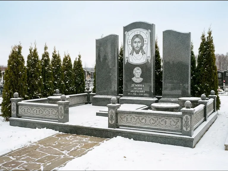 Памятник с гравировкой иконы: узкая вертикальная стела-пилон с ликом — икона в резной рамке-киоте, открытая лужайка без ограды, работа «Одинцов» в Норильске