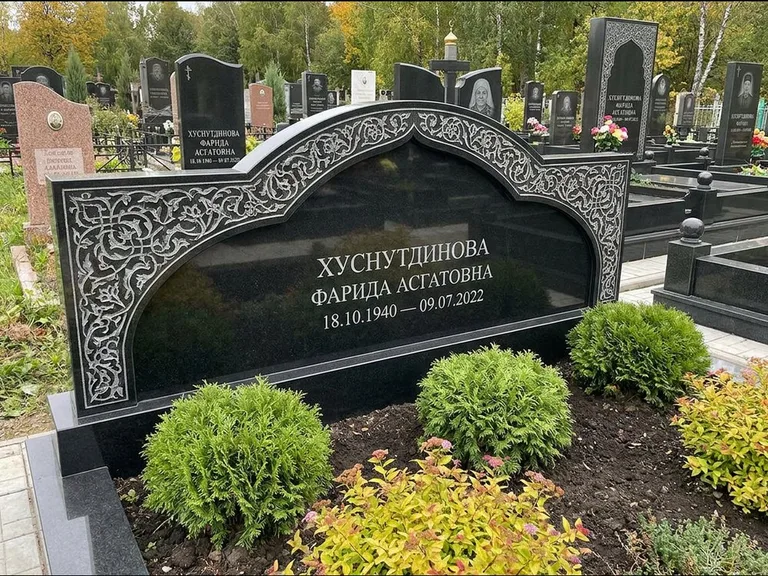 Мусульманский памятник: вытянутая горизонтальная семейная стела с аркой — белая гравировка силуэта мечети с минаретами, участок с декоративными кустами, работа «Зарипова» в Норильске