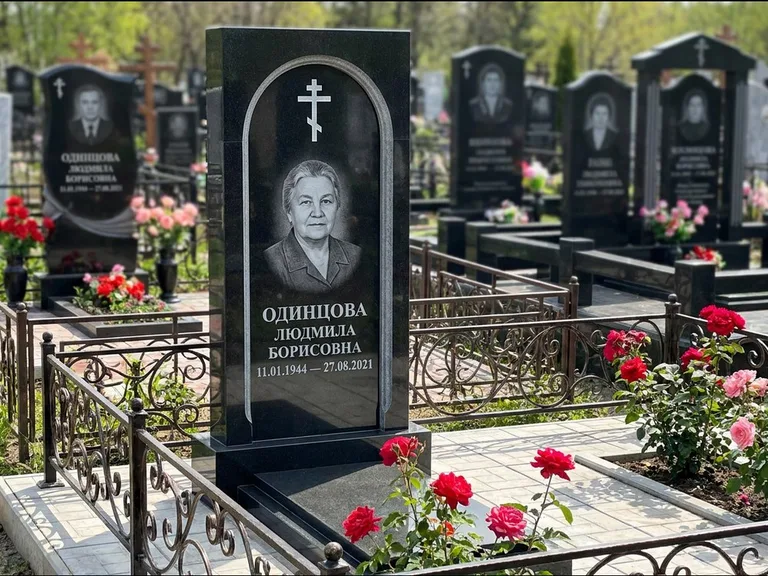 Памятник из чёрного гранита — скромная невысокая стела с крестом с терновым венцом, работа «Лаврентьева» в Норильске