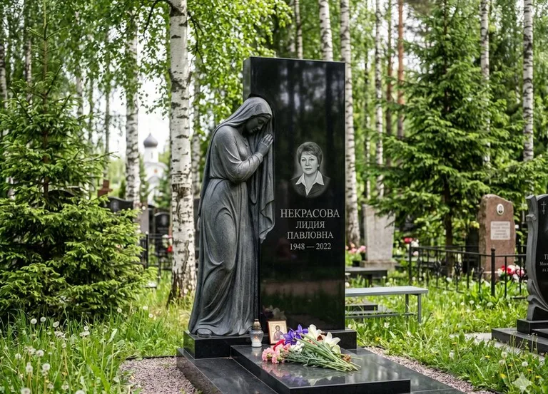 Гранитная фигура скорбящего мужчины у чёрной стелы в Норильске